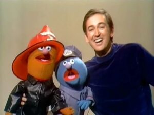 an orange muppet fireman with a blue muppet policeman with a man, Bob from Sesame Street